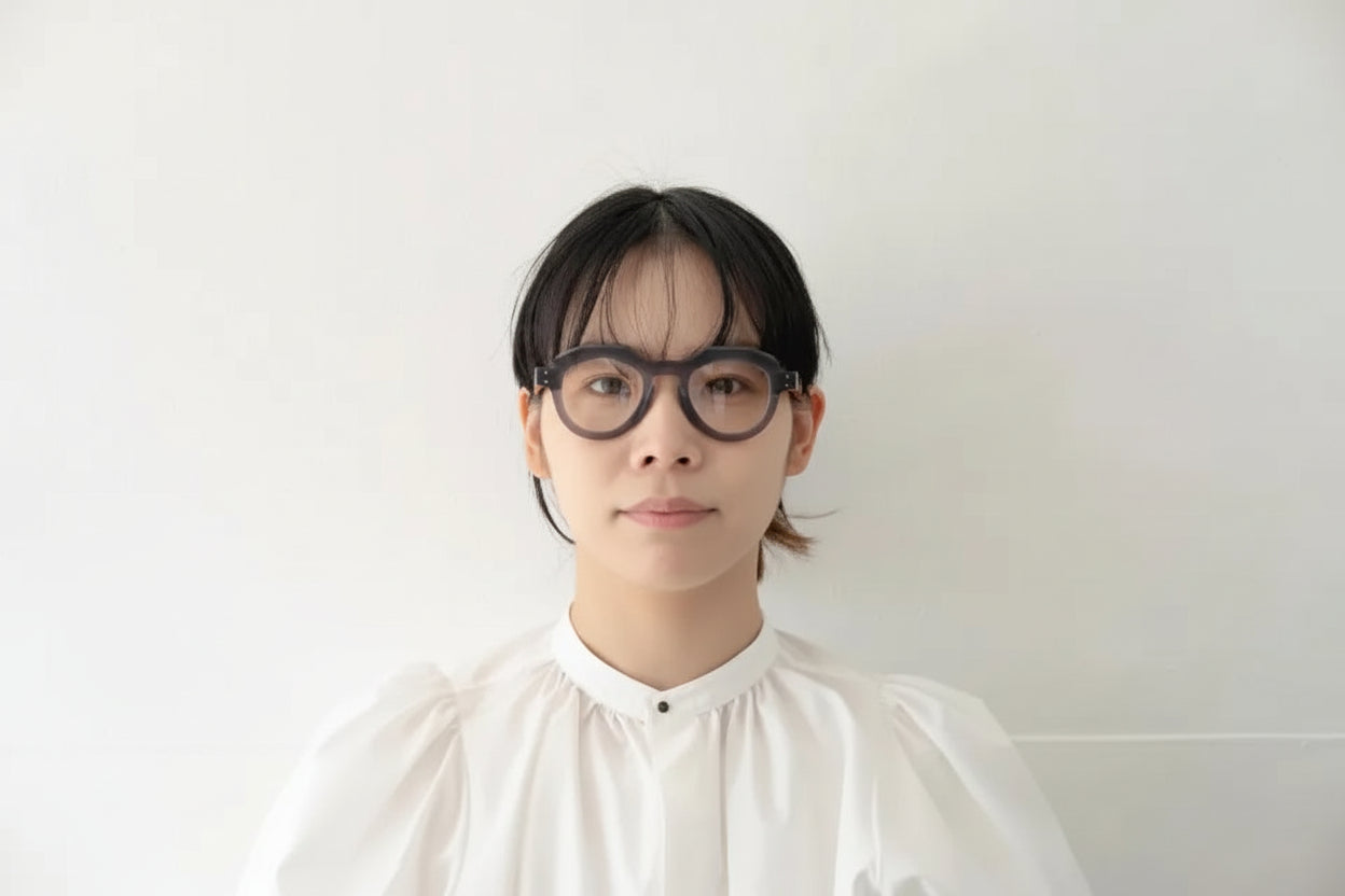 Person wearing a white shirt and blue glasses against a plain background