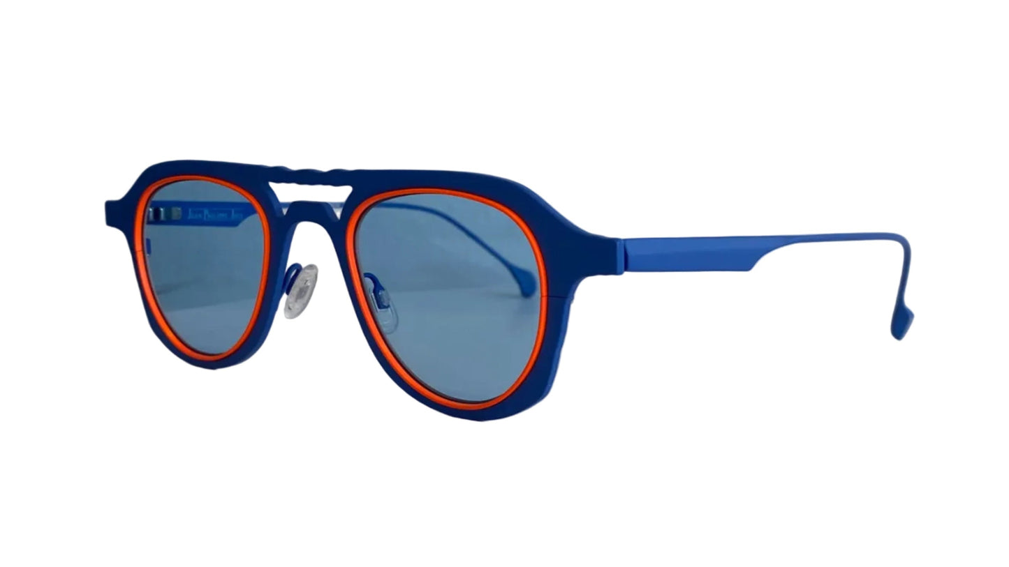 Blue and orange-framed sunglasses with light blue lenses, resting on a white surface against a white wall.