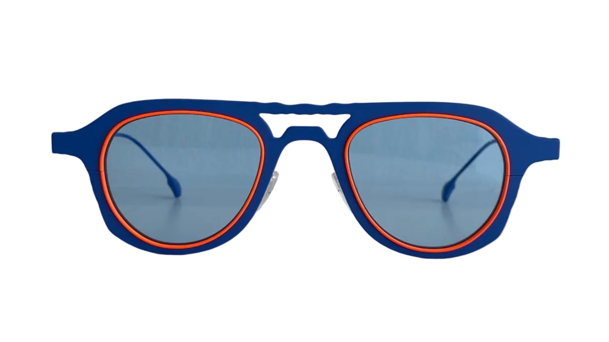 Blue artistic aviator frame sunglasses with a thin orange inner rim and light blue lenses, resting on a white surface against a white wall.