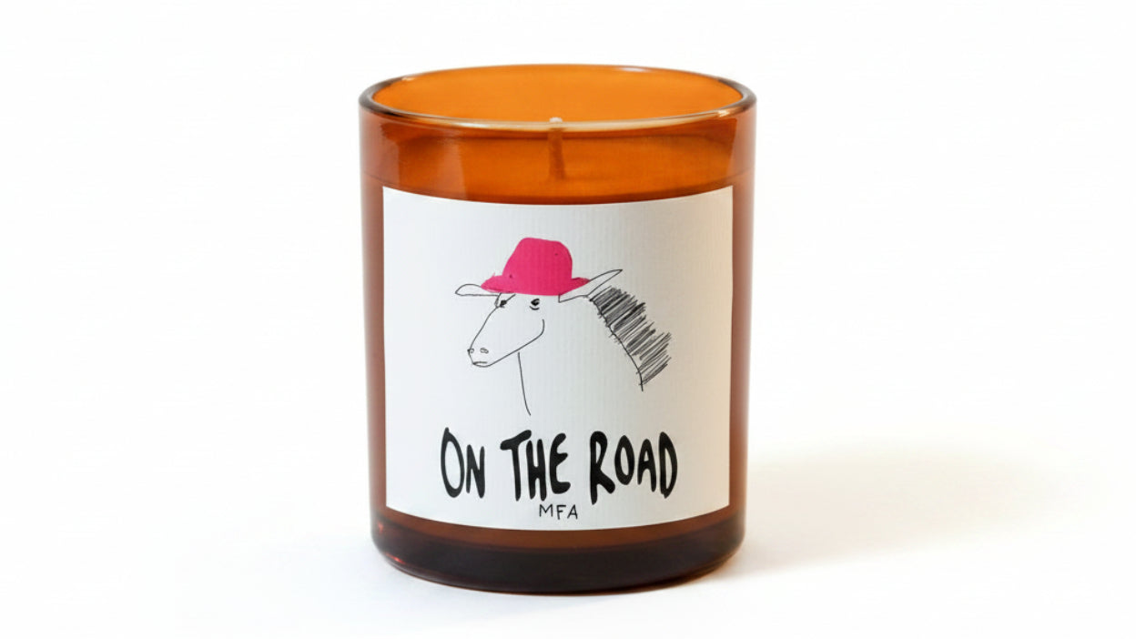 Candle with a label featuring a horse illustration and text 'On The Road MFA' on a peach background