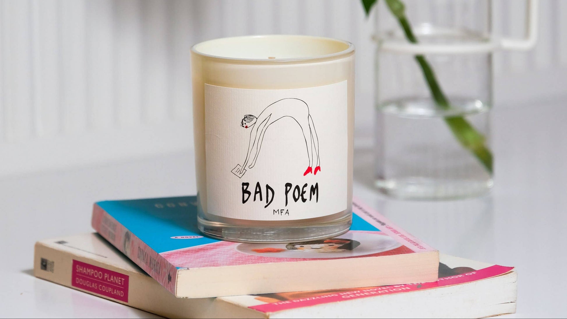 Candle labeled 'Bad Poem' on a stack of books with a vase in the background