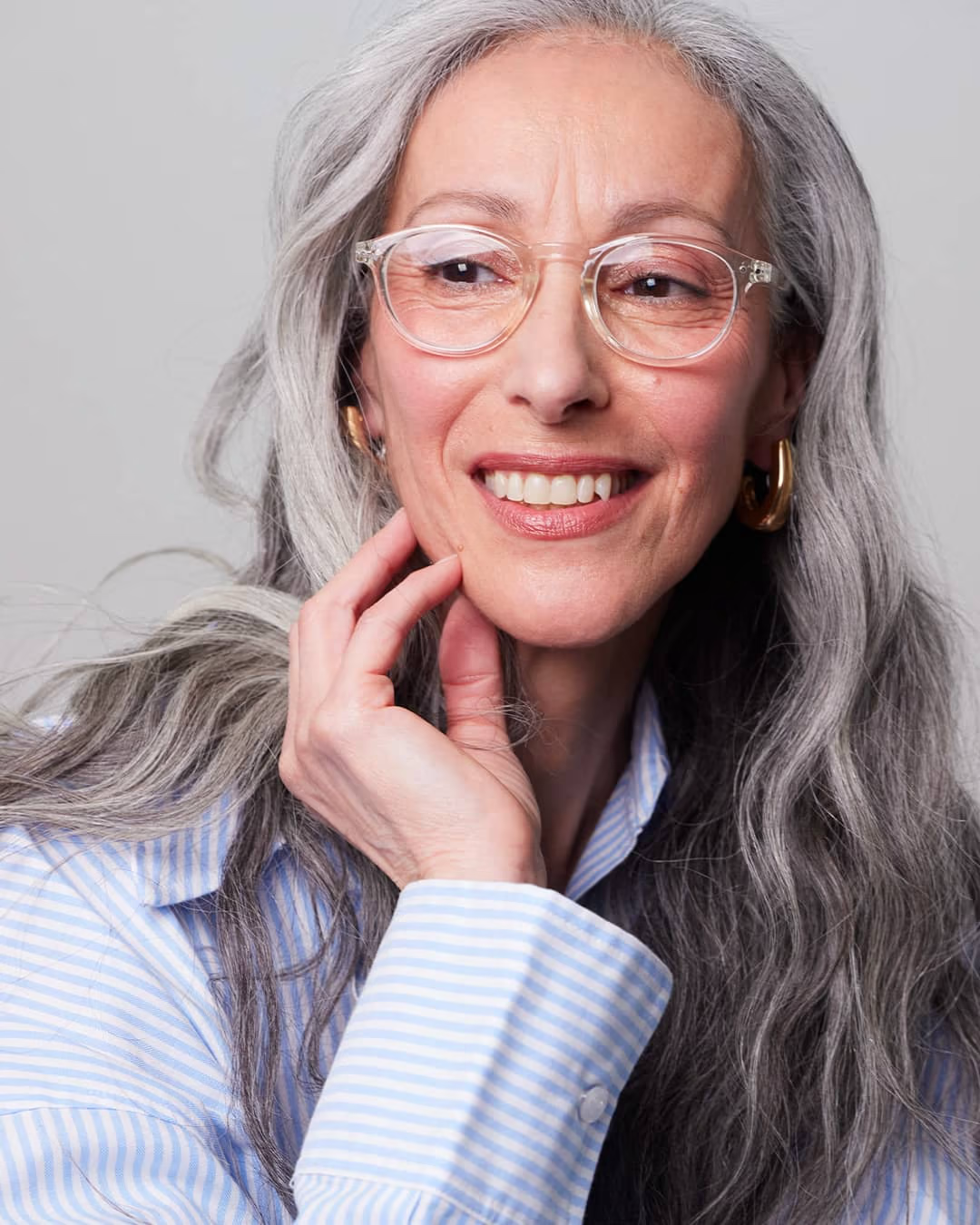 Woman with gray hair wearing glasses and a striped shirt against a plain background