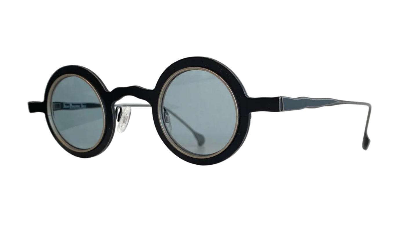 Round black eyeglass frames with light blue-tinted lenses, resting on a white surface against a white wall.